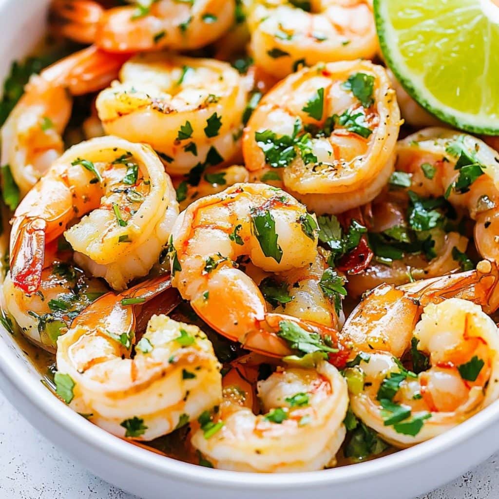 Peeled and deveined shrimp cooked in cilantro and lime juice served in a white bowl.