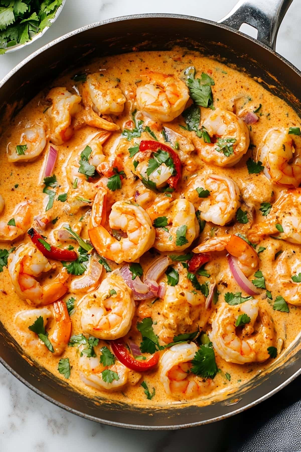 A skillet of creamy chipotle shrimp with onions and red bell peppers, garnished with chopped cilantro.