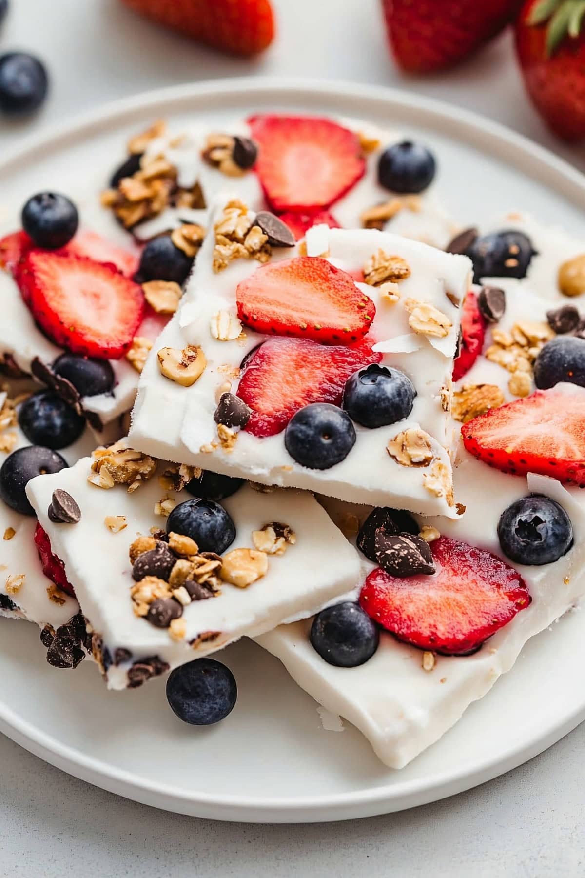 Frozen yogurt bark pieces stacked on a plate, featuring a mix of fresh fruit, nuts, and chocolate chips.