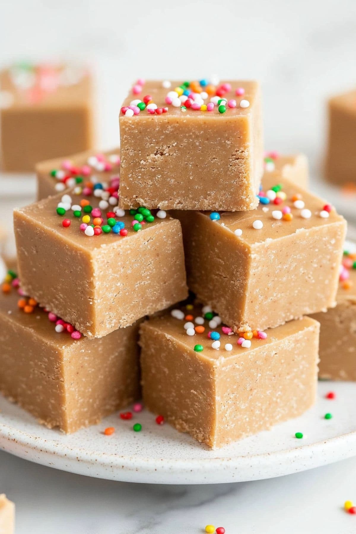 Cubes of gingerbread fudge with candy sprinkles stacked on a white plate.