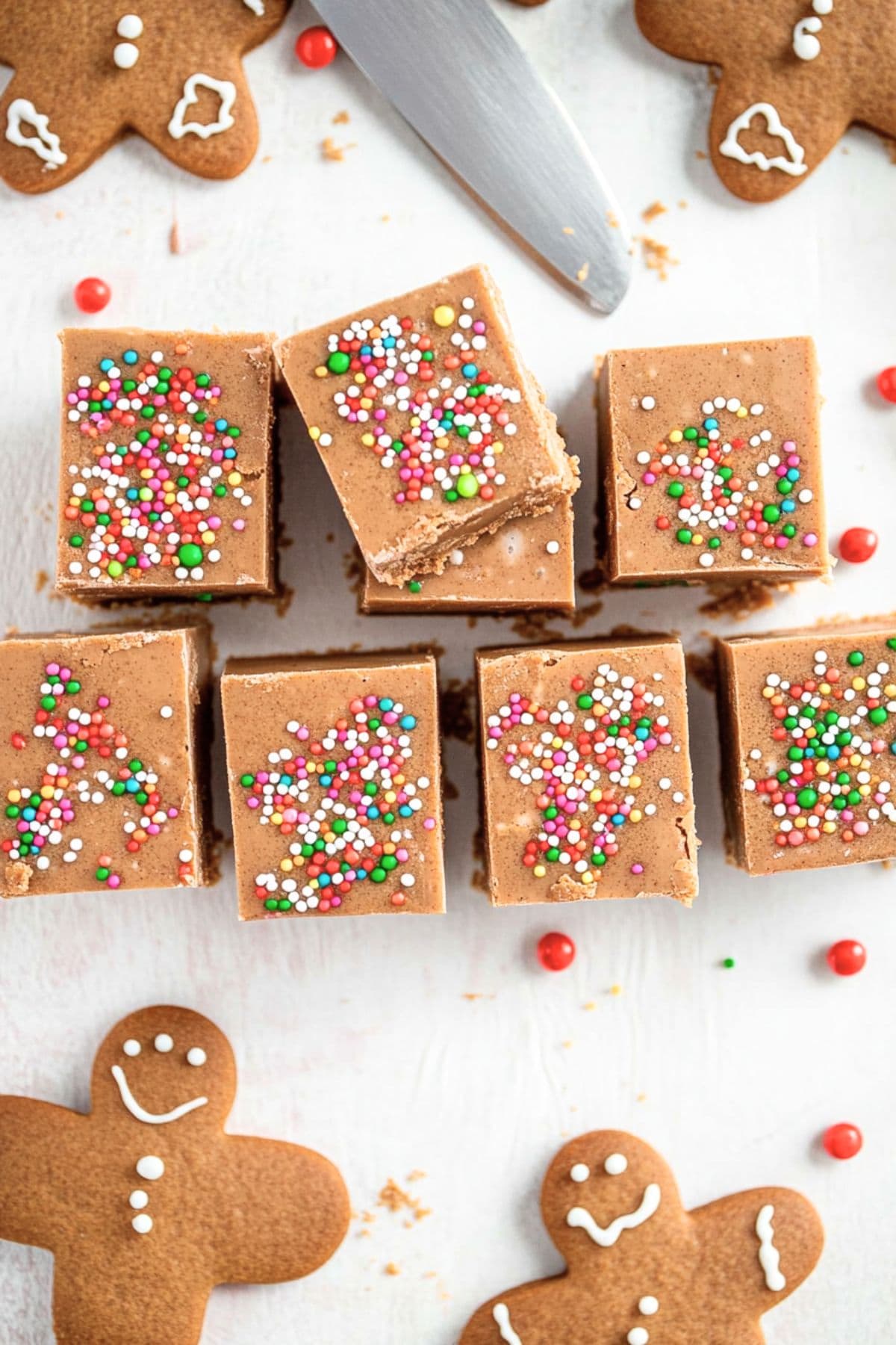 Gingerbread fudge pieces  with candy sprinkles on a table with gingerbread cookies, top view