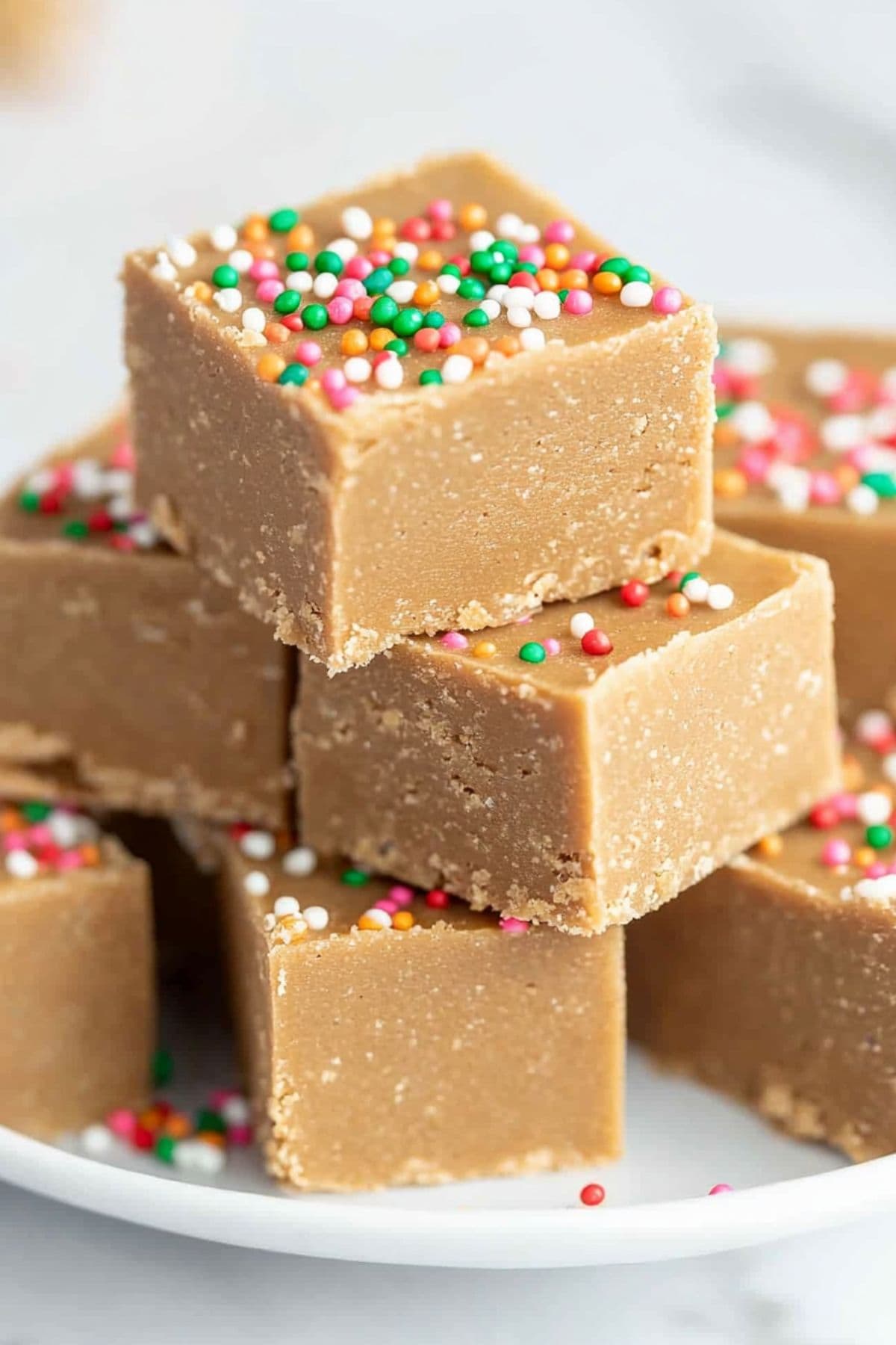 Bite-size pieces of gingerbread fudge with candy sprinkles arranged on a white plate, side view