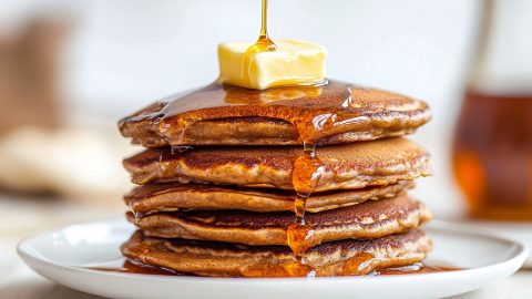 A stack of fluffy gingerbread pancakes drizzled with maple syrup and topped with butter.