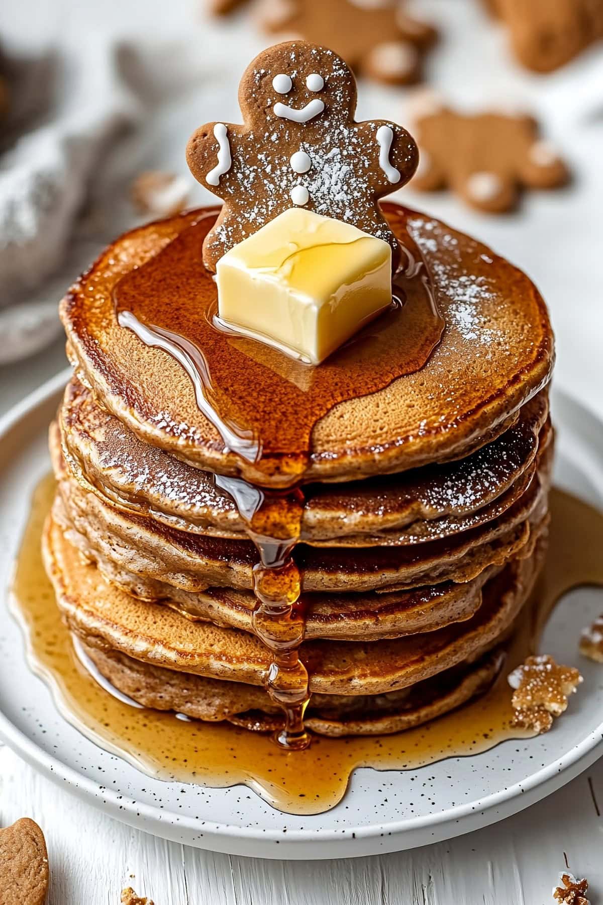 A stack of gingerbread pancakes topped with butter, maple syrup and a gingerbread cookie.