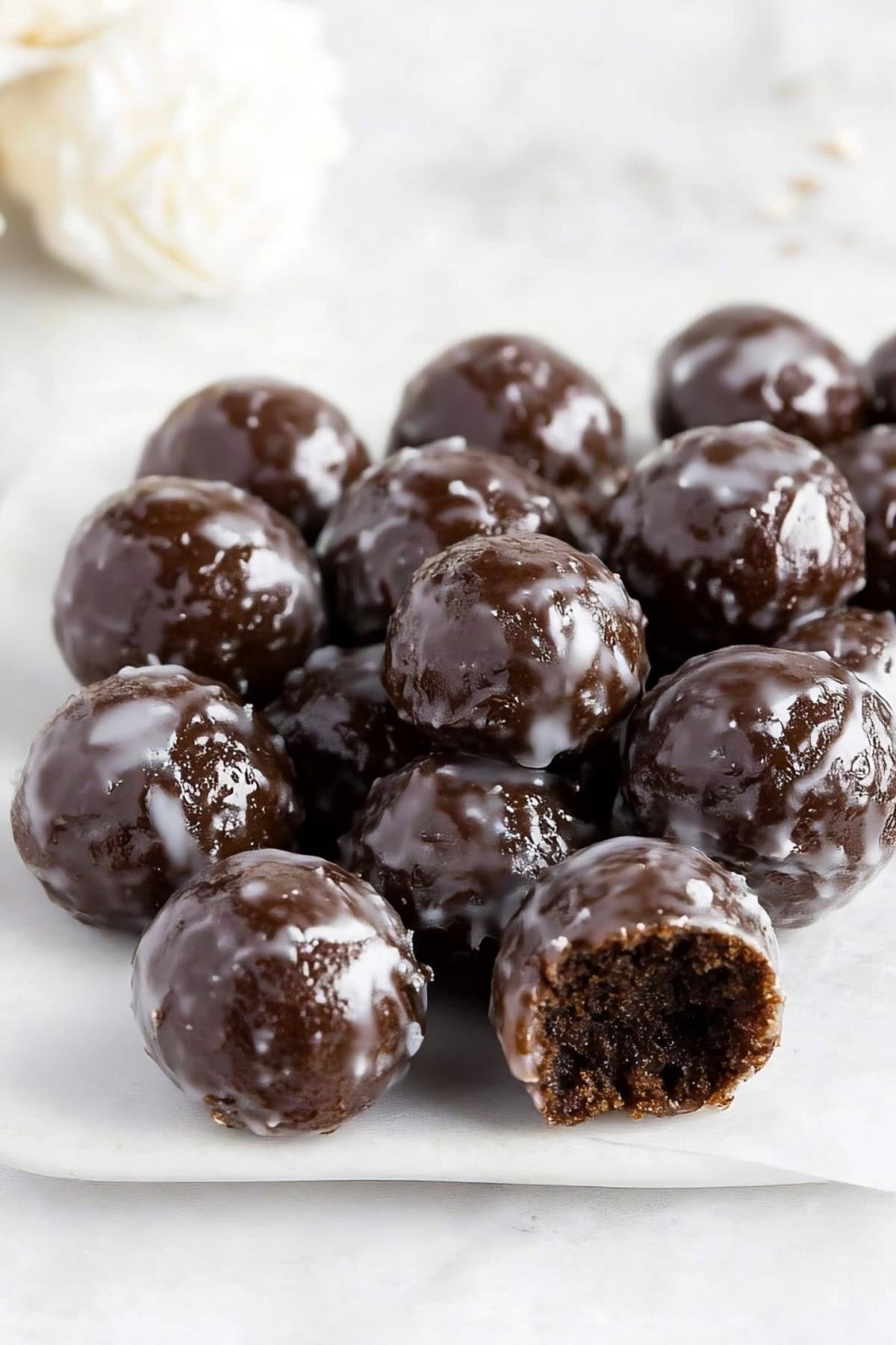 Homemade vanilla glazed chocolate donut holes on parchment paper.