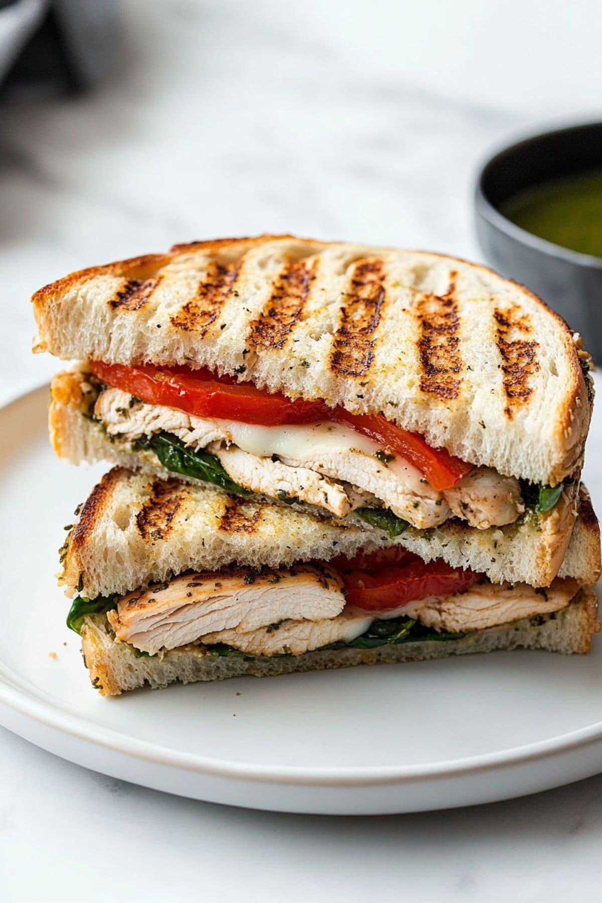 Grilled chicken panini sandwich sliced in half with fresh tomato, baby spinach and mozzarella cheese.