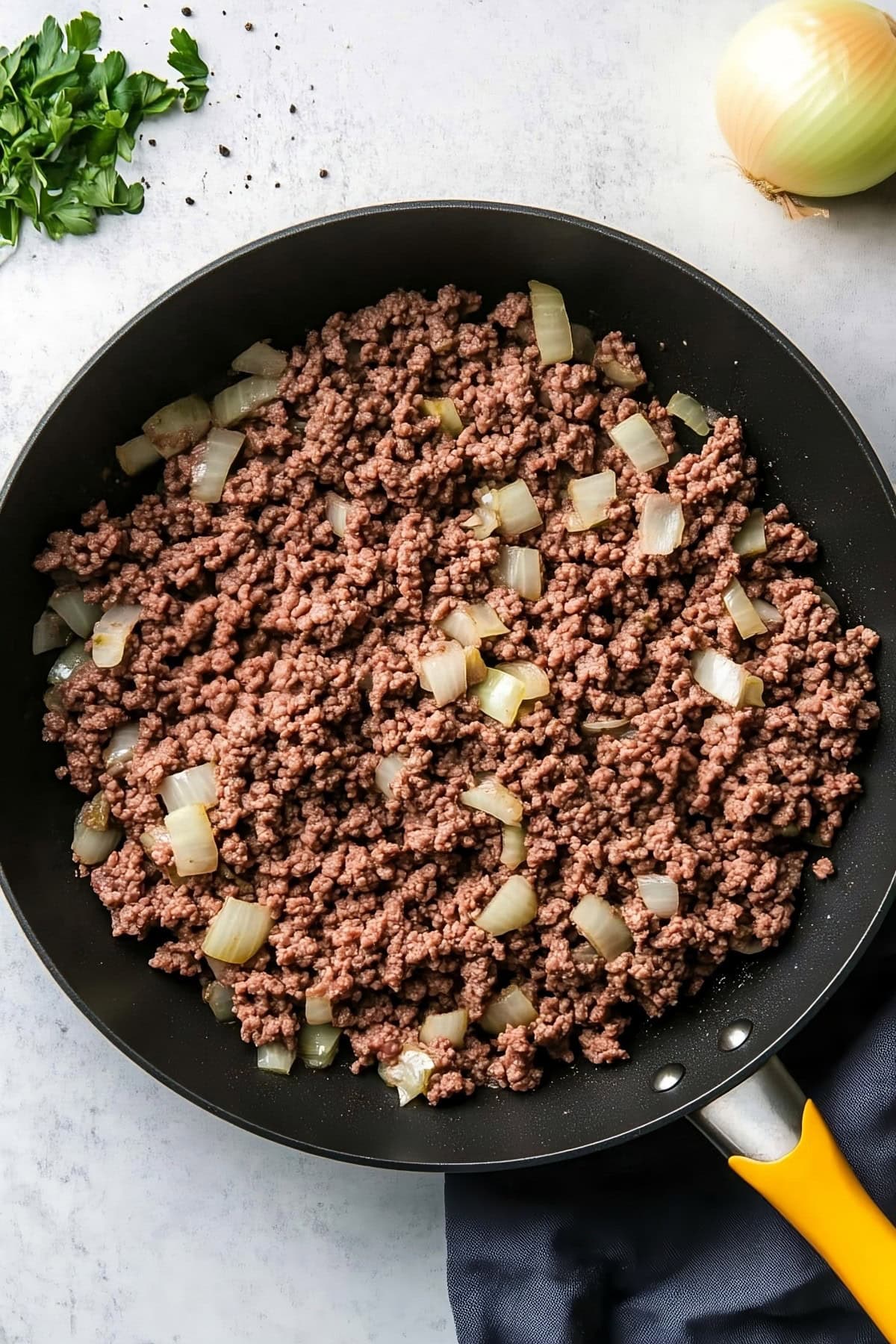 Ground beef with onions in a black skillet, overhead view.