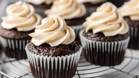 Bunch of chocolate cupcake garnished with whipped cream arranged in a cooling rack.