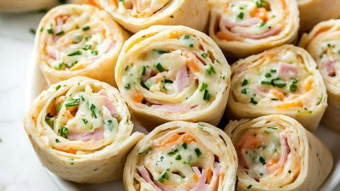 A stack of ham and cheese pinwheels on a white plate, ready to serve.