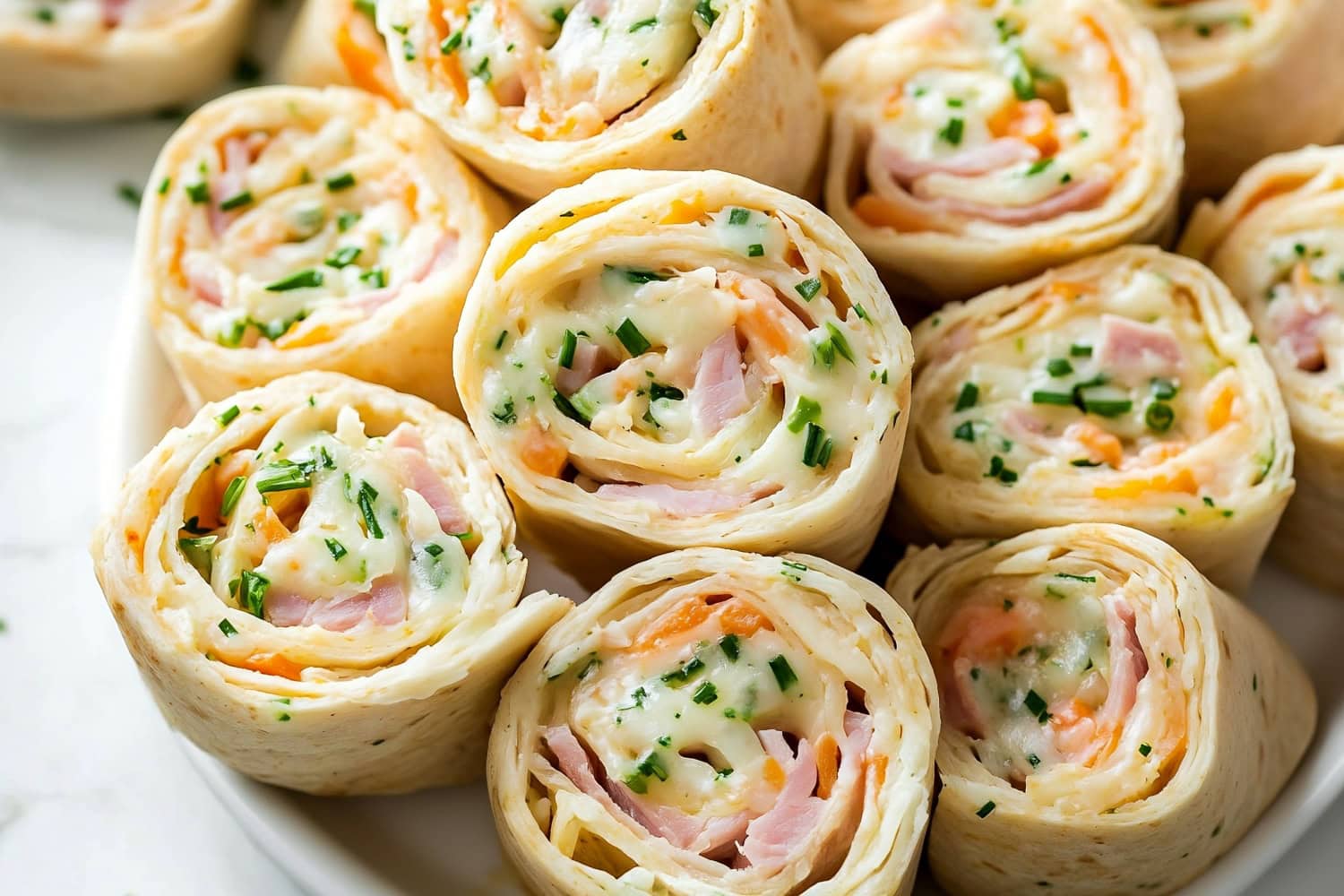 A stack of ham and cheese pinwheels on a white plate, ready to serve.