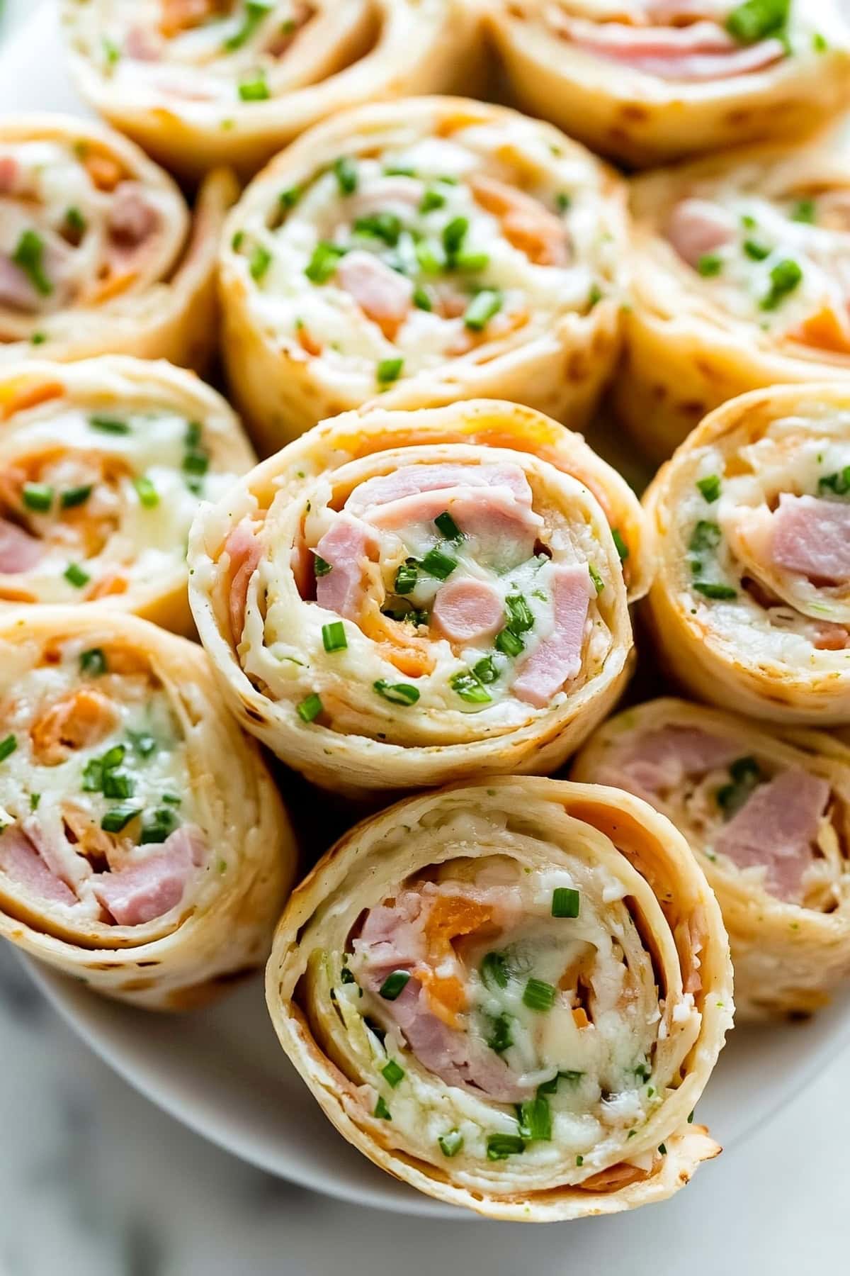 Overhead view of ham and cheese pinwheels with chopped green chives.