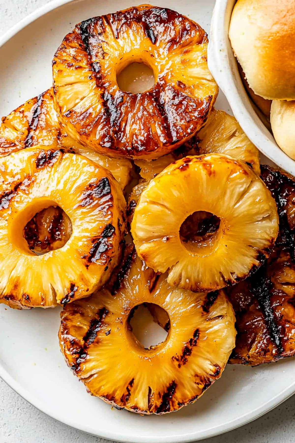 Plater of grilled pineapples and a bowl of buns.