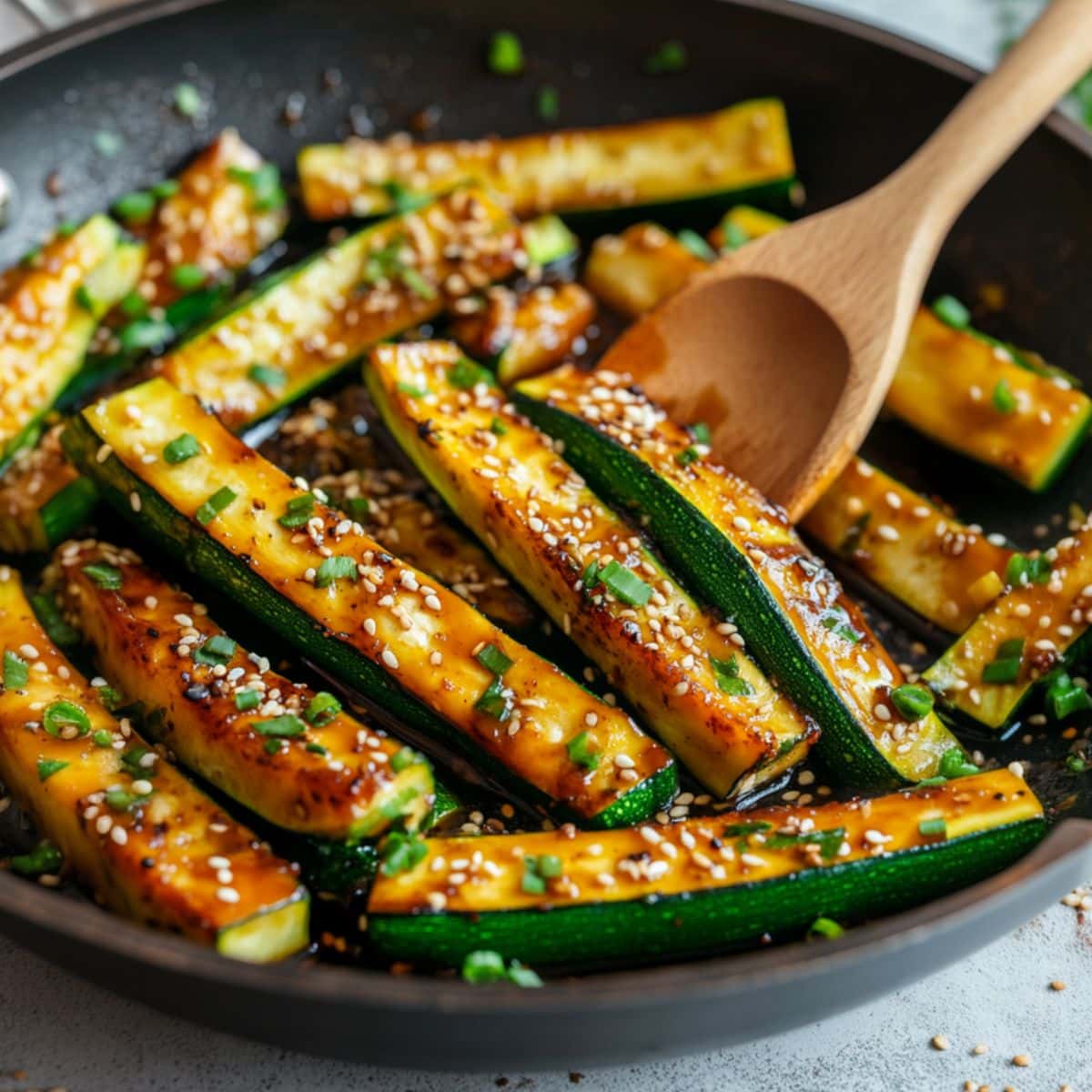 Hibachi zucchini tossed in a wok pan with a wooden ladle.