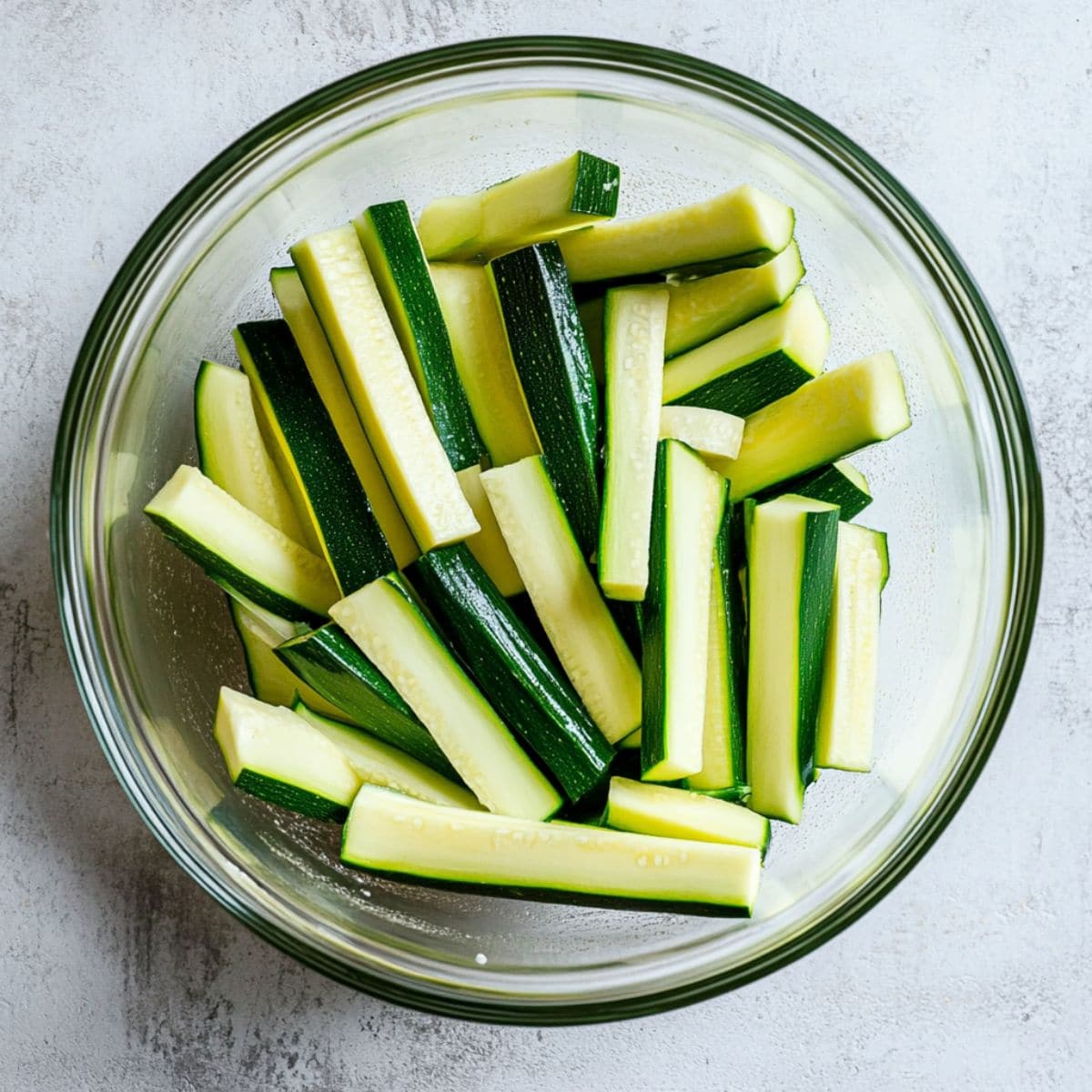 Zucchini sticks in a large glass mixing bowl.