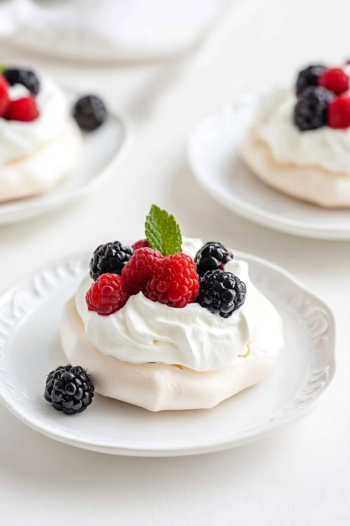 A mini pavlova on a white plate topped with a swirl of whipped cream and a variety of fresh berries.