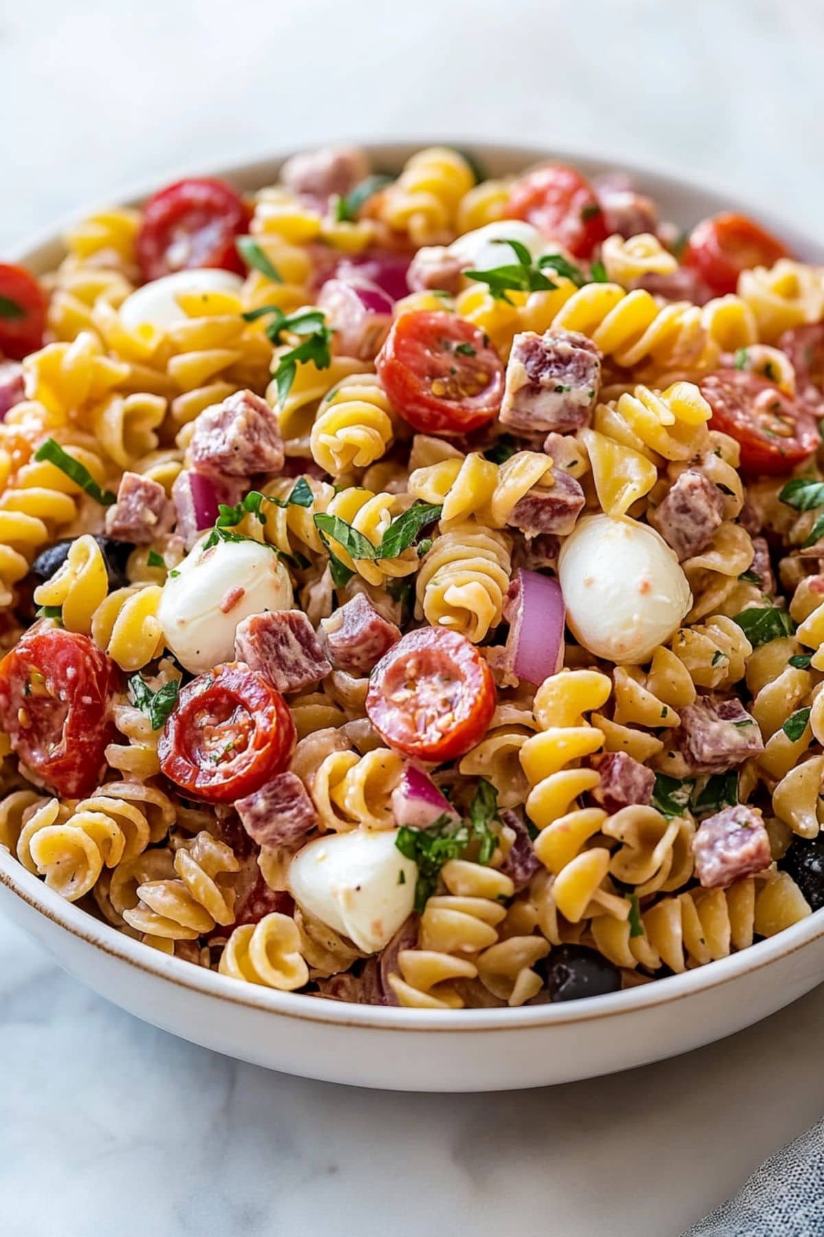 Italian pasta salad made with rotini pasta, tomatoes, mozzarella, salami, and herbs.