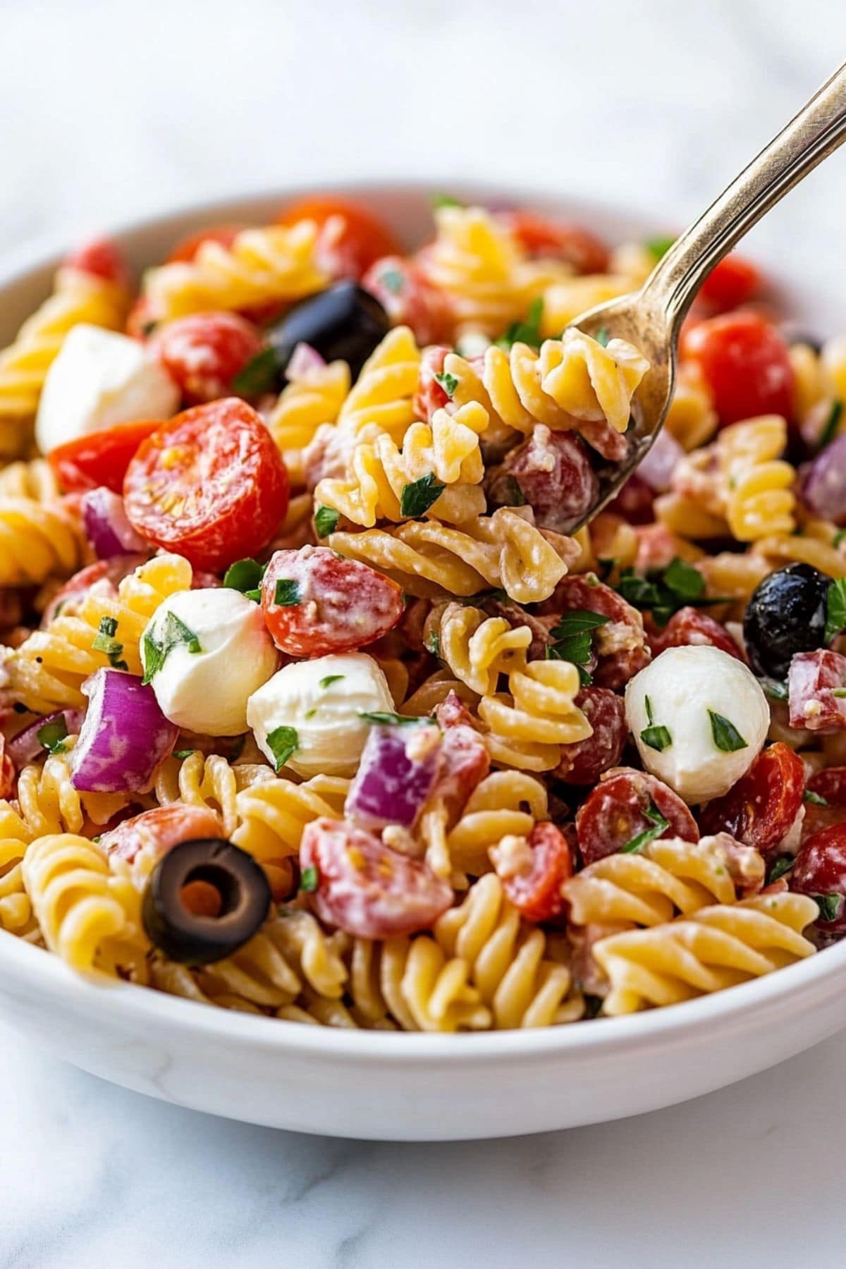 Spoon scooping a serving of Italian pasta salad served in a white bowl.