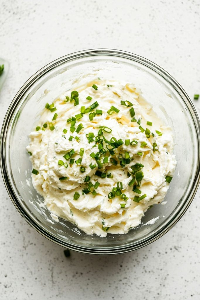 Softened cream cheese with garlic powder and green onions in a glass mixing bowl. 