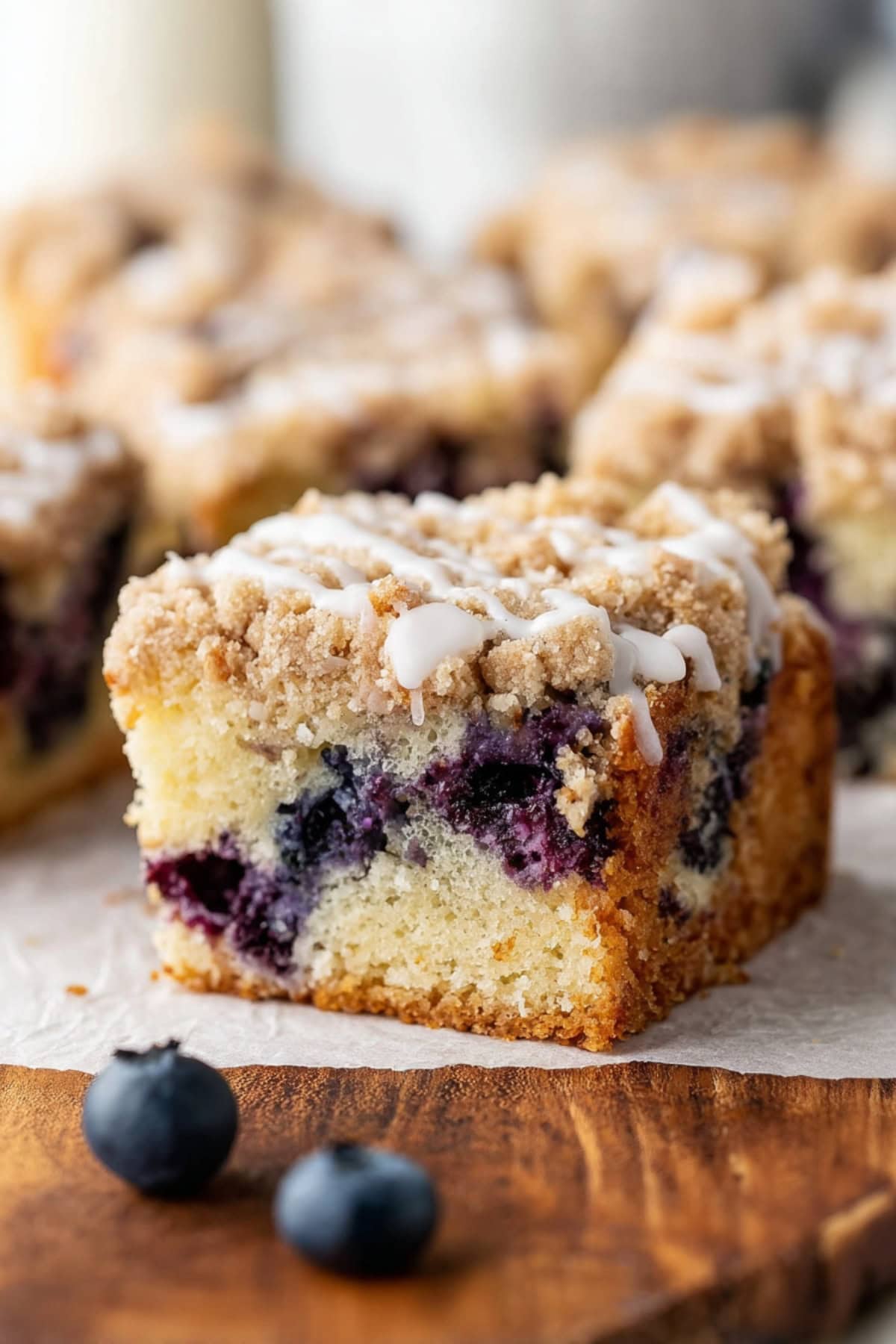 Lemon blueberry coffee cake topped with a light drizzle of white icing, with fresh blueberries in the foreground.