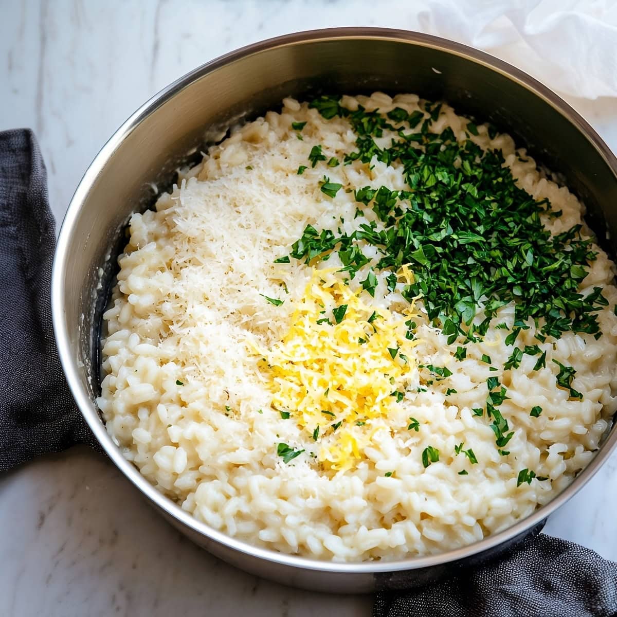 A large sauce pan of arborio rice, lemon zest, grated parmesan and chopped parsley.