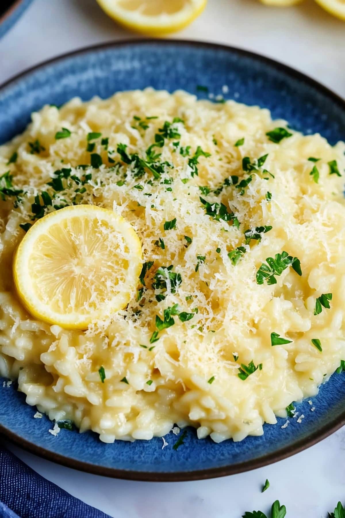 Creamy lemon risotto garnished with fresh parsley, parmesan, and a slice of lemon, served in a blue plate, close up