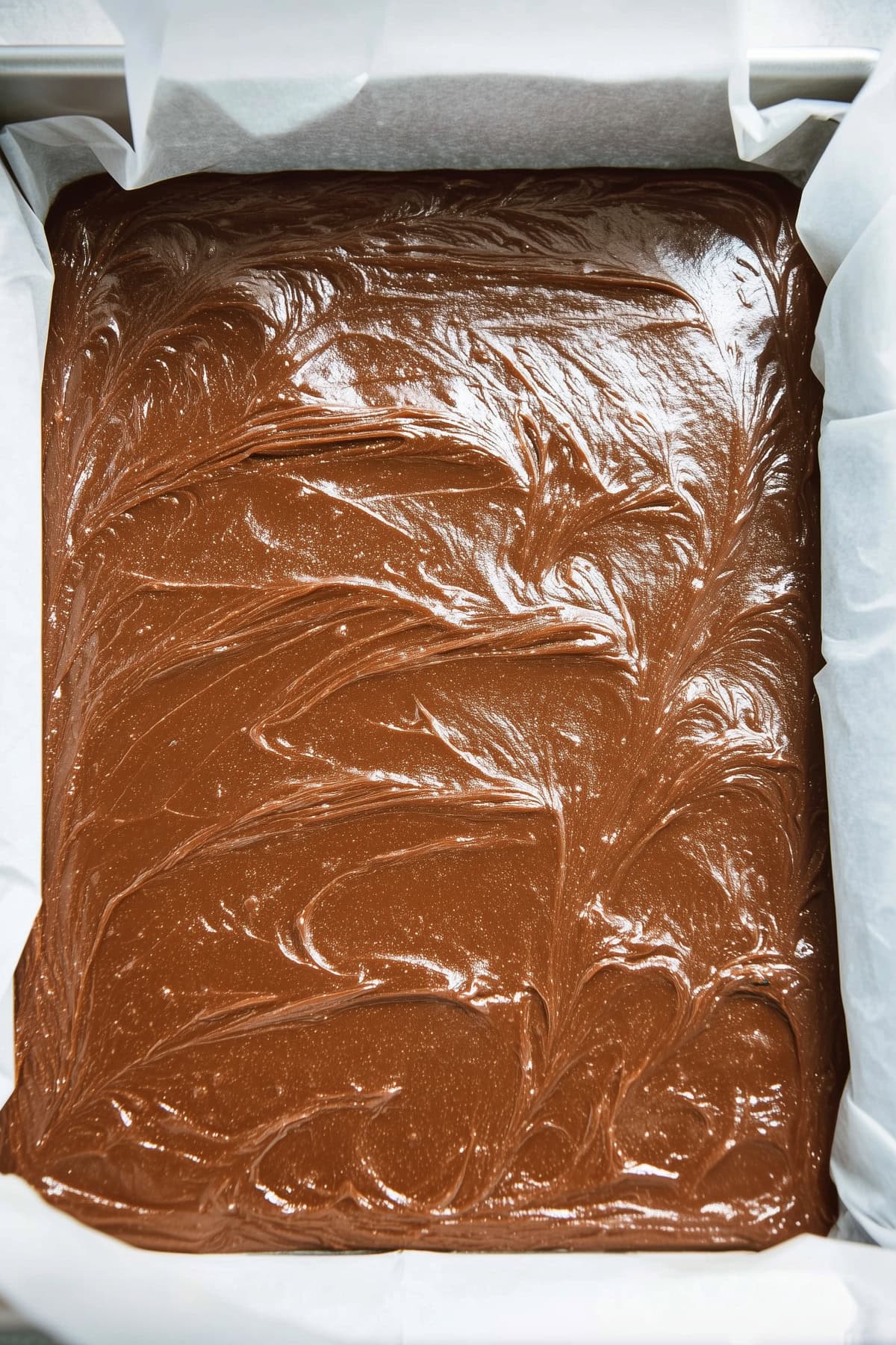 A baking pan lined with parchment paper filled with smooth chocolate brownie batter.
