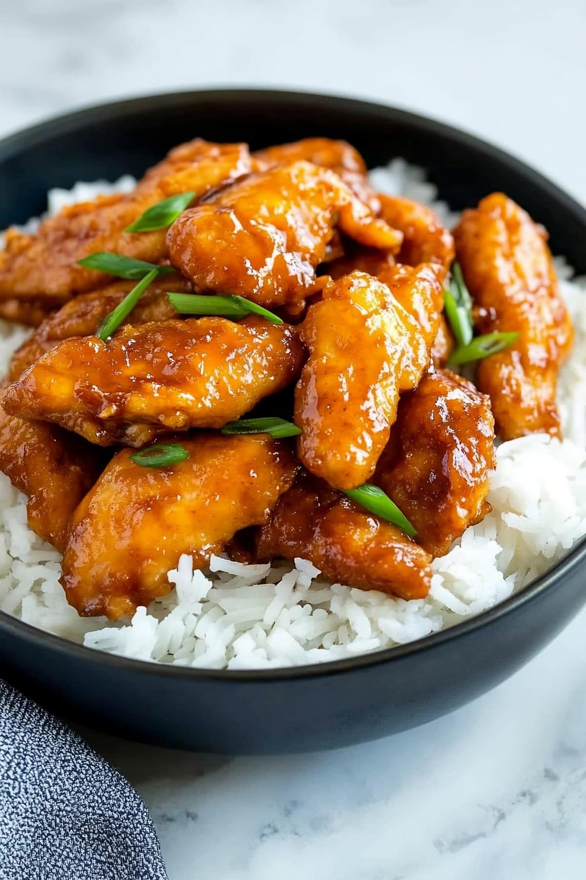 A black bowl of Mongolian chicken with chopped onions.