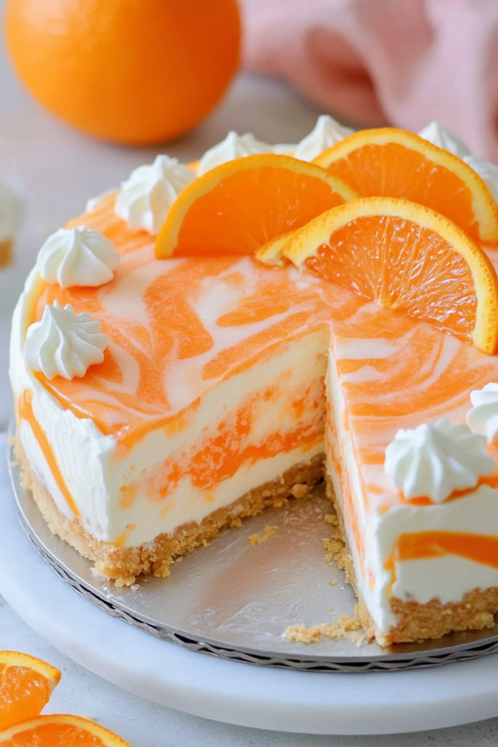 Sliced whole no bake orange creamsicle cheesecake garnished with whipped cream and slices of orange, close up.