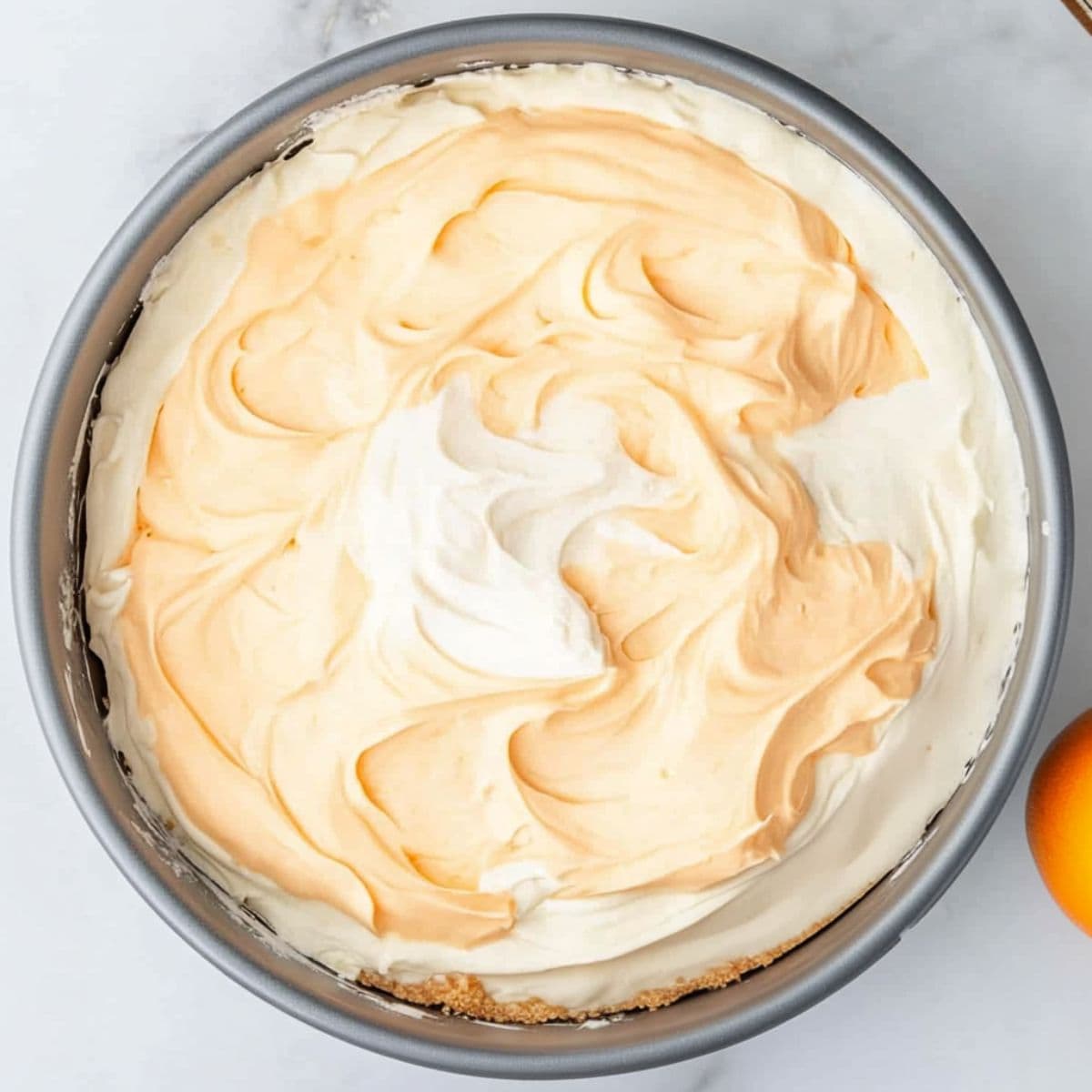 Orange creamsicle cheesecake filling on top of graham crust in a springform pan, top view.