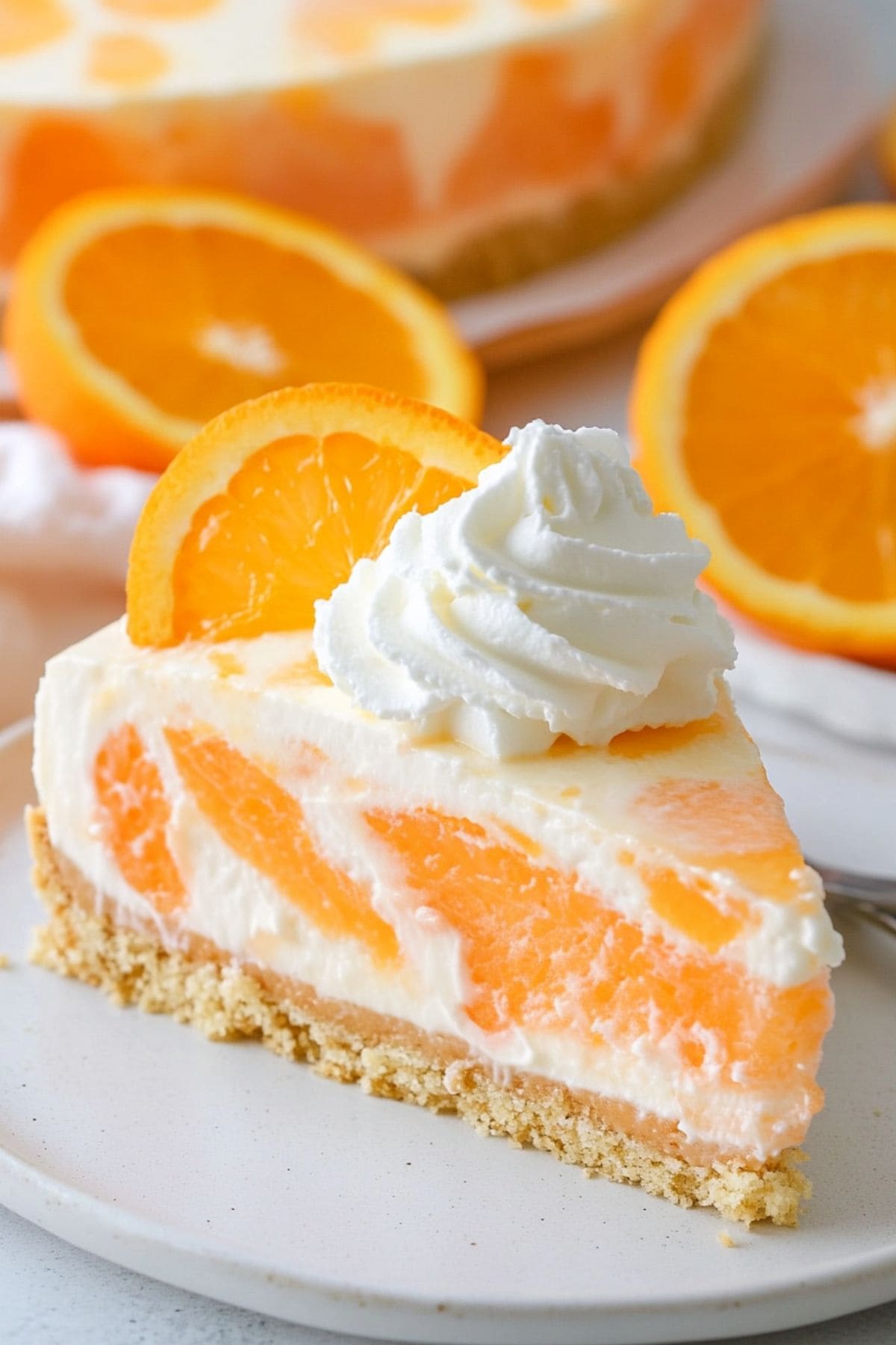 Slice of orange creamsicle cheesecake served on a white plate garnished with whipped cream and orange slice.