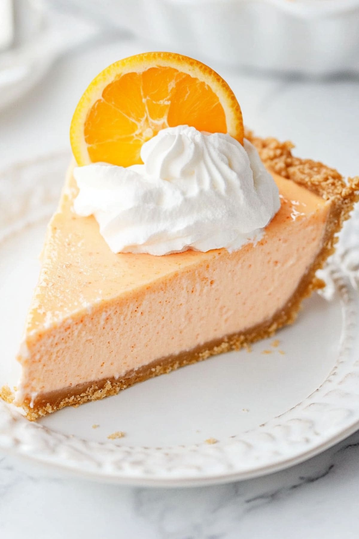 A slice of no-bake orange creamsicle pie with whipped cream and an orange slice on a white plate