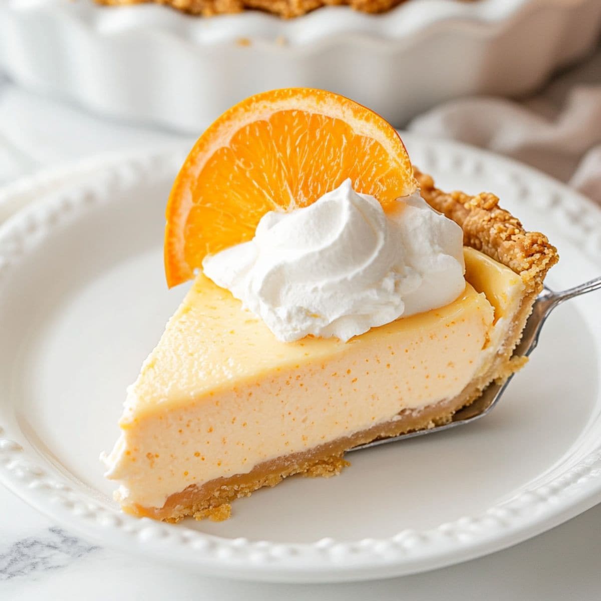 Orange creamsicle pie slice garnished with whipped cream and orang slice in a pie ladle. 