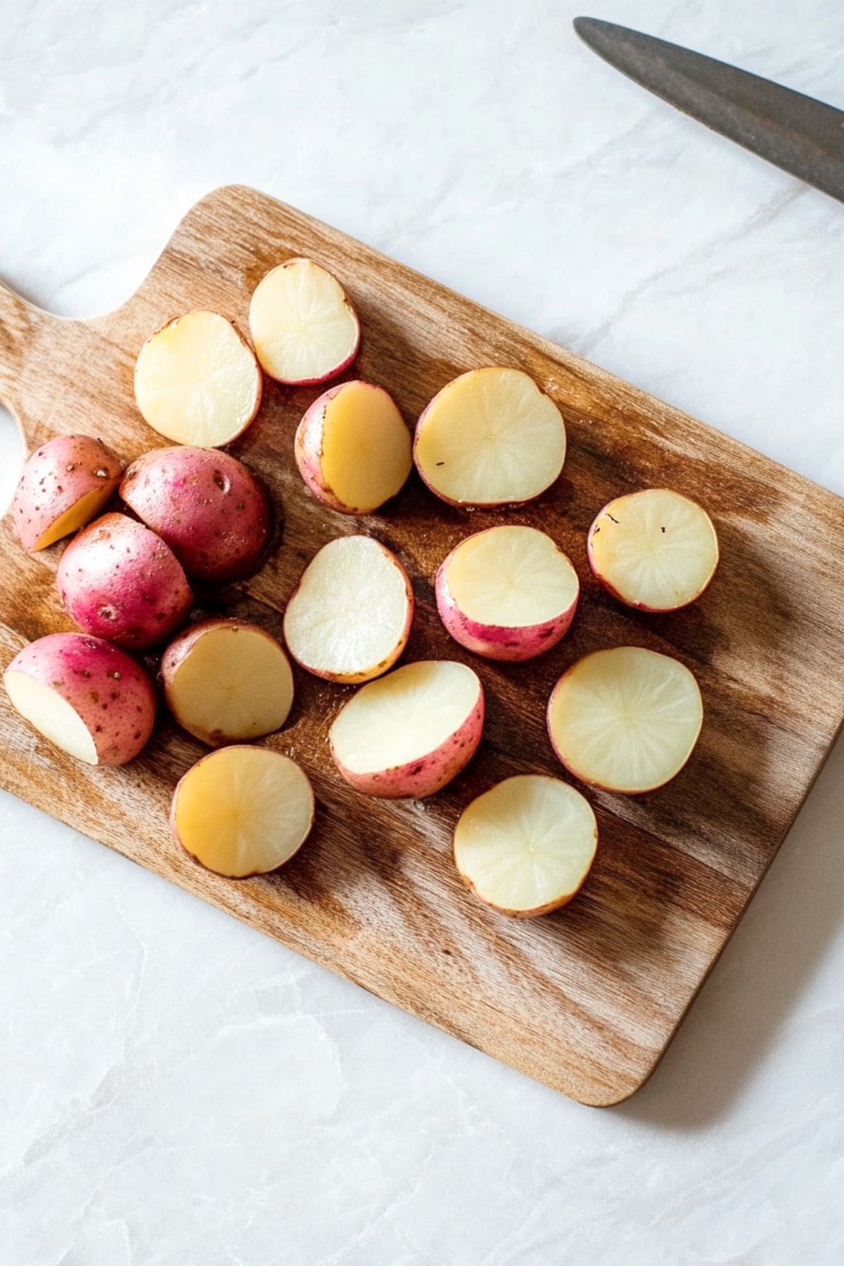 Baby red potatoes sliced in half on a wooden chopping board.