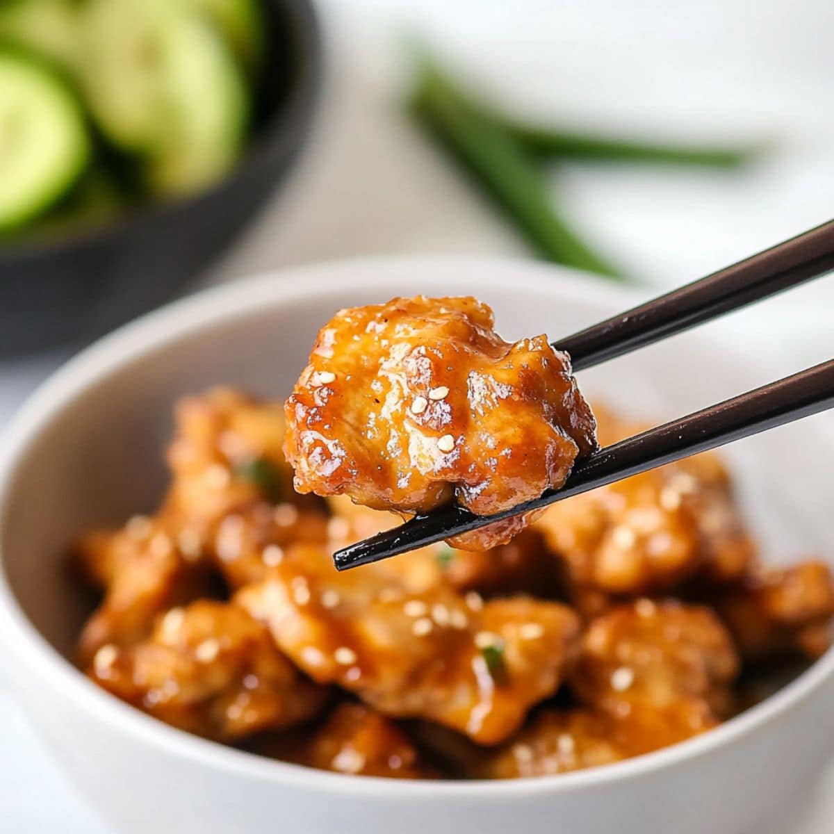 Chopsticks holding a piece of chicken coated in sauce.