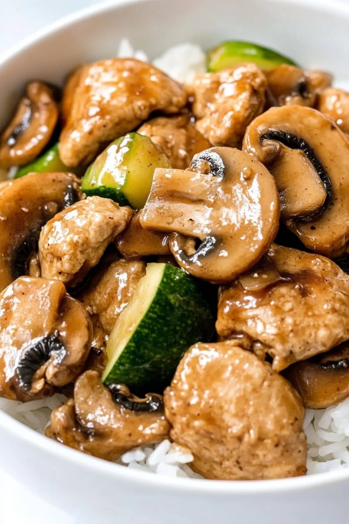 Panda express mushroom chicken served on top of white rice in a white bowl.