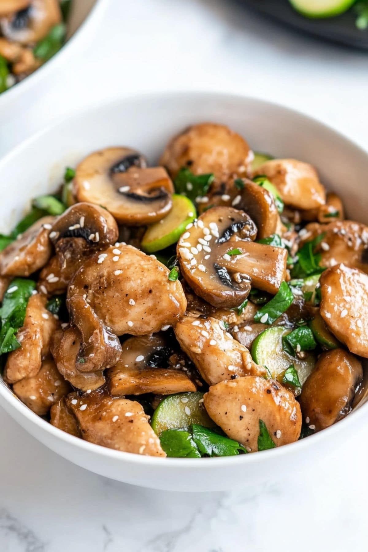 Chicken with mushroom and sliced zucchini coated in umami sauce served on a white bowl.