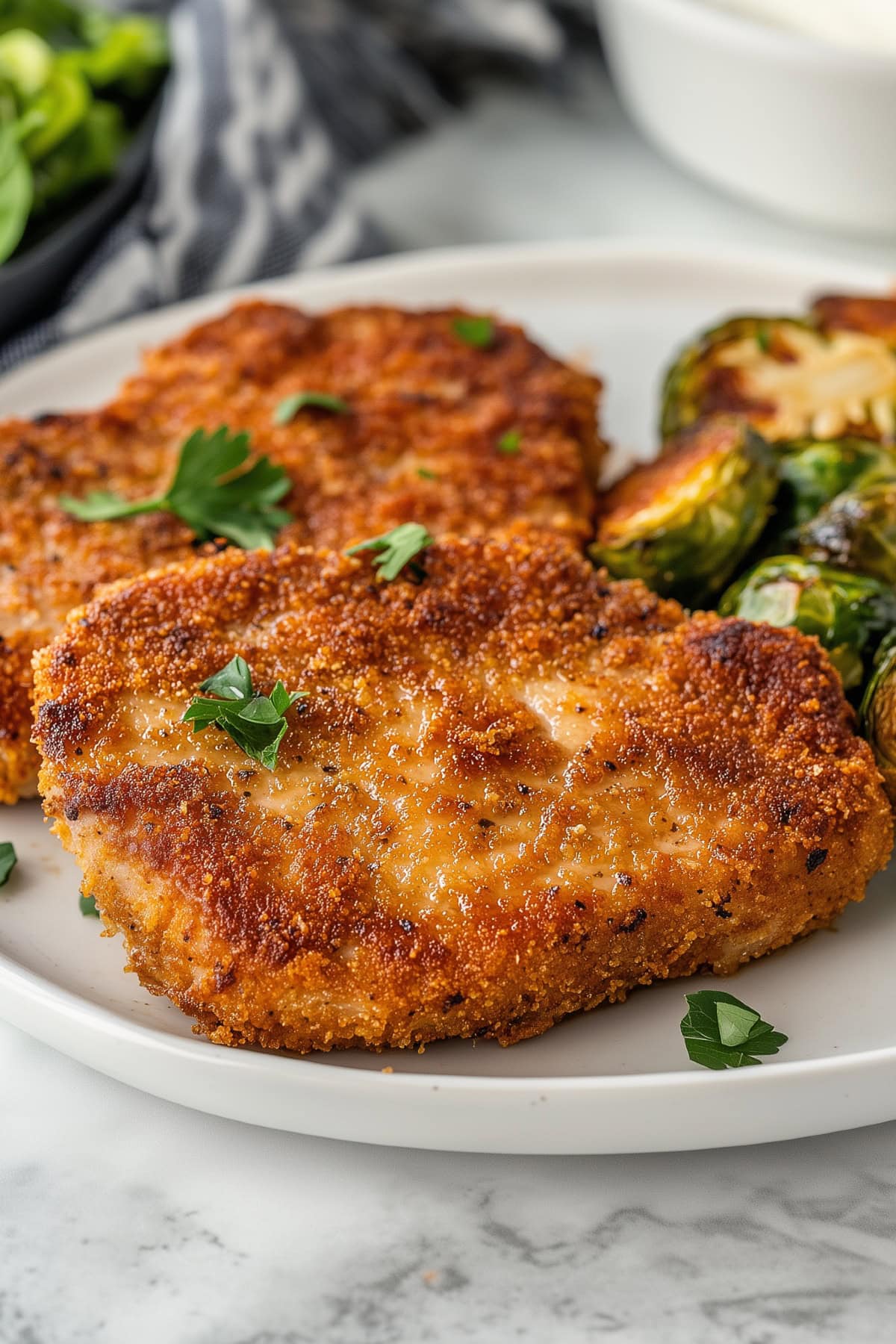 A plate of parmesan crusted pork chops with a sprinkle of fresh herbs.