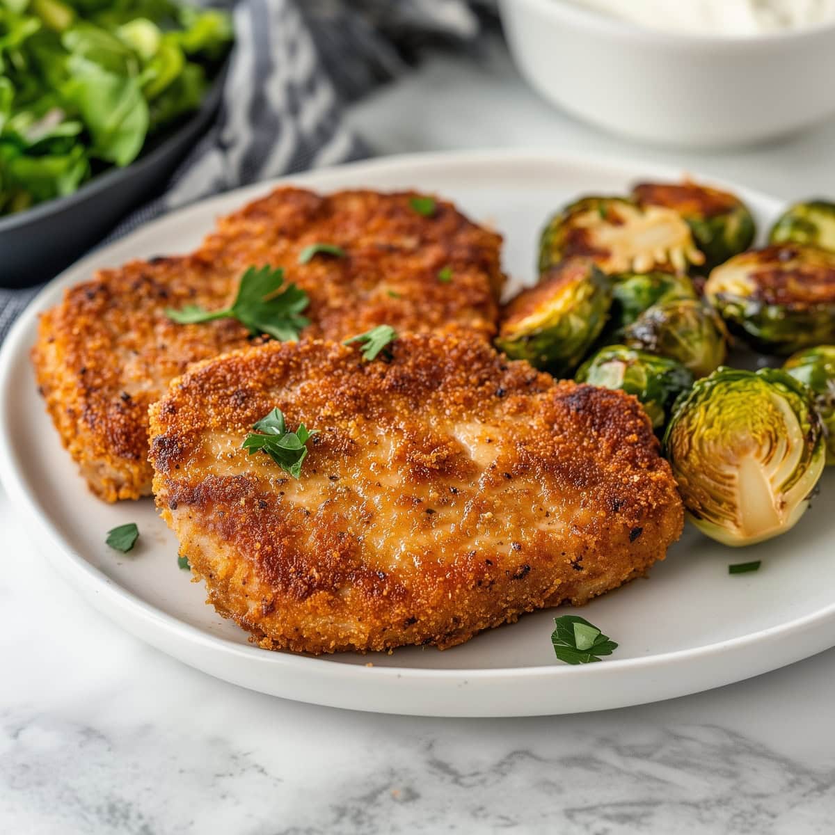 A plate of parmesan crusted pork chops served with roasted brussels sproutes.