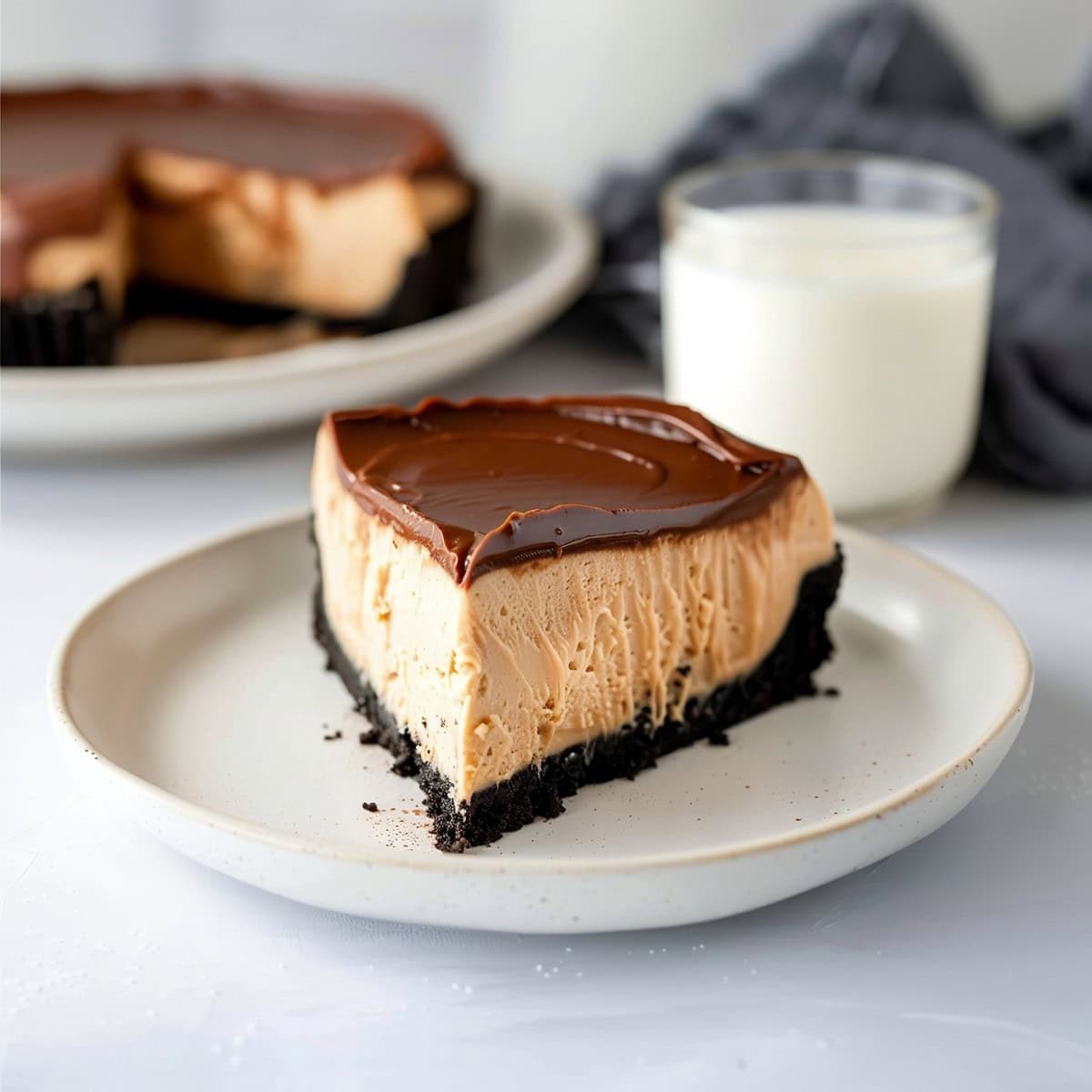 Delicious peanut butter cheesecake, sliced on a plate, with the whole cake and a glass of milk in the background