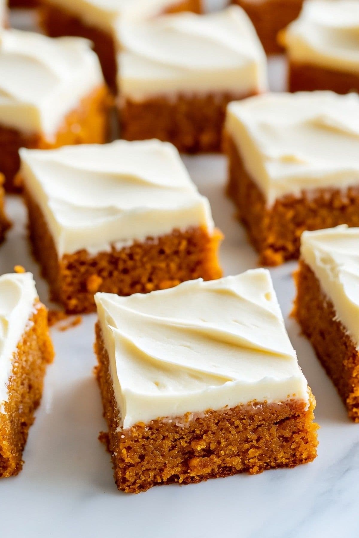 Pumpkin bars with cream cheese frosting on a white marble surface.