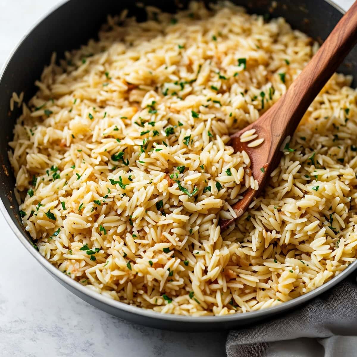 A deep skillet of rice pilaf on a white marble table.