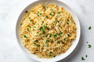 A serving of golden rice pilaf on a white plate with a sprig of parsley.