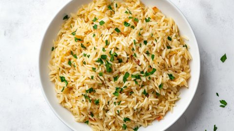 A serving of golden rice pilaf on a white plate with a sprig of parsley.