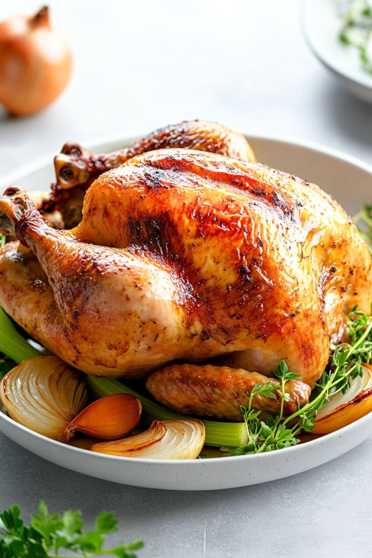 Whole roast chicken served in a plate with onions and celery stalk.