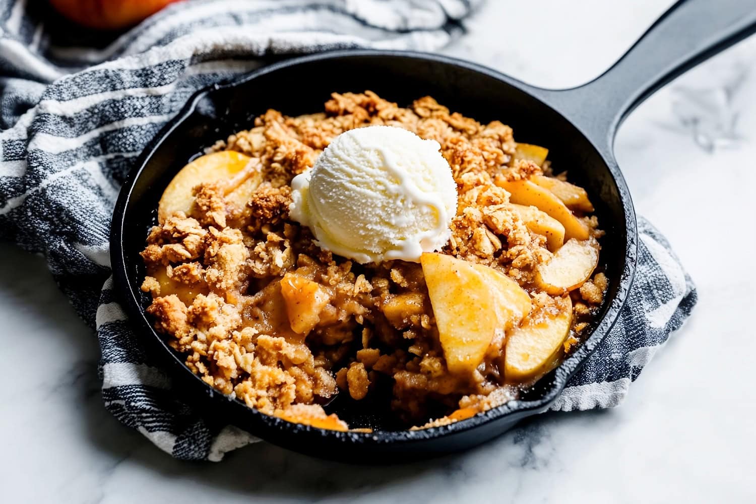 Angled view of skillet apple crisp with a scoop of ice cream on top.