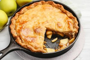 Rustic skillet apple pie cooling on a wooden table.