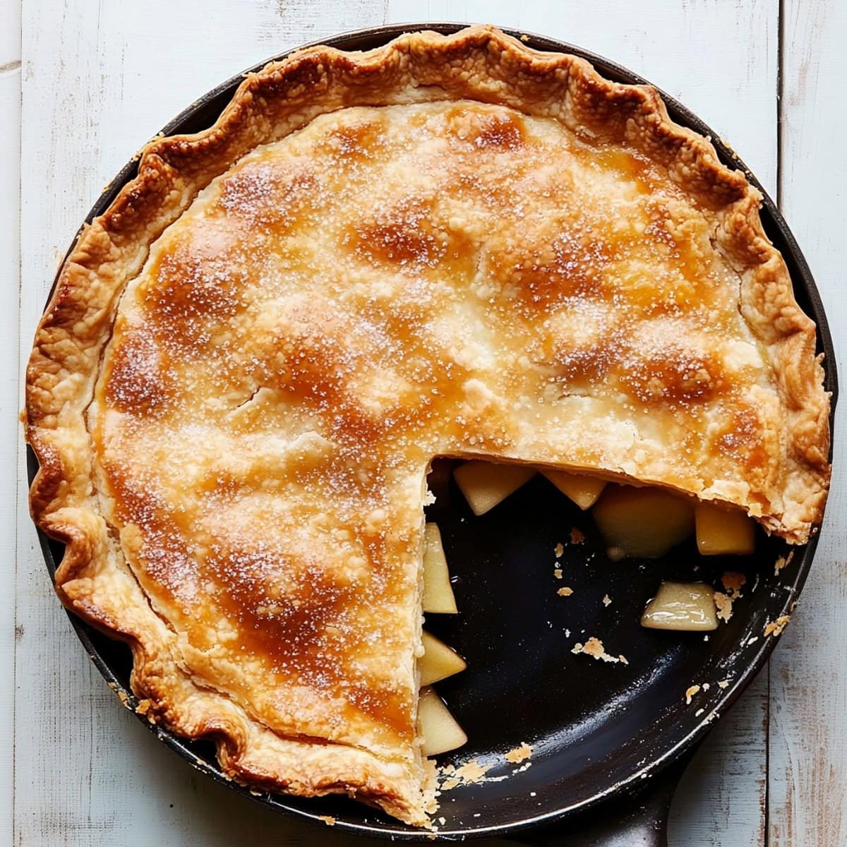 Golden-brown skillet apple pie with a flaky crust and a slice removed, top view