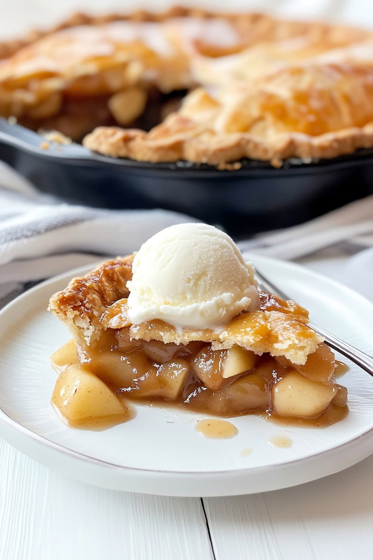 Slice of killet apple pie topped with ice cream on a white plate. 