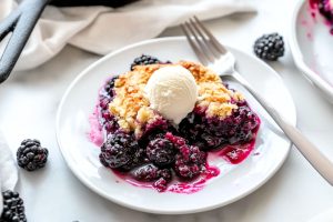 Skillet blackberry cobbler garnished with a scoop of vanilla ice cream served in a white plate.