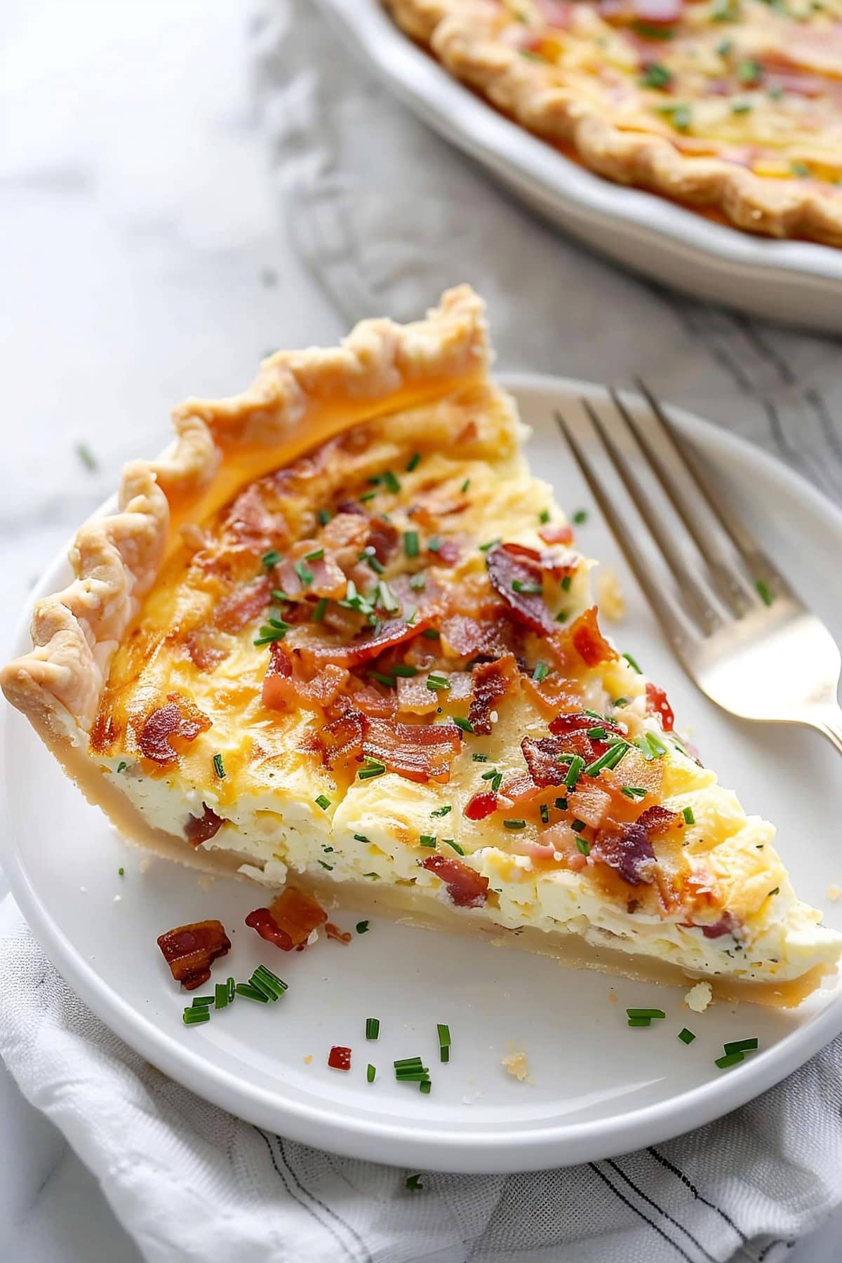 Slice of Quiche Lorraine with bacon, green onions and cheese on a white plate with a fork on the side